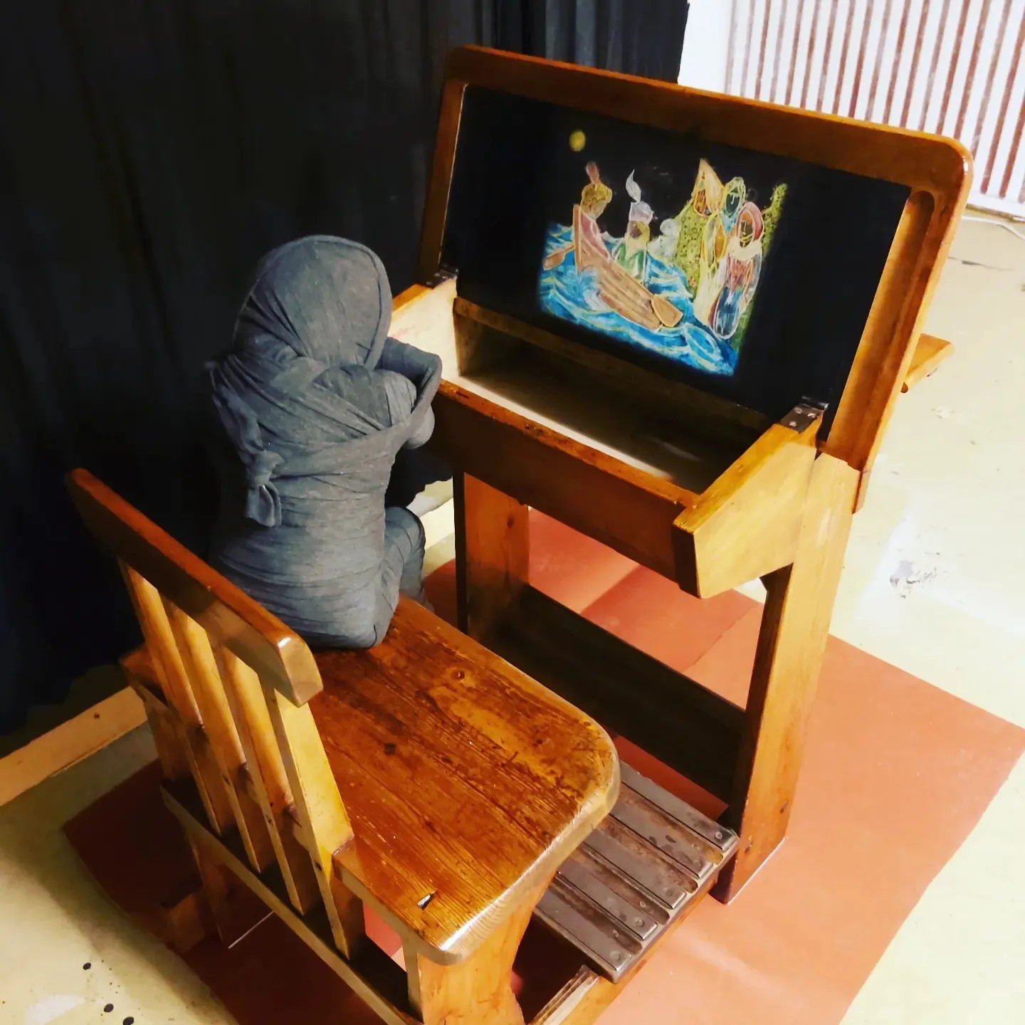 "Ruth On Yksin." 80X60X70 installaatio, entisöity lasten pulpetti, käsin tehty nukke, metallirunko, kipsi, mustat käärinliinat, liitupiirros "uni". 790e
